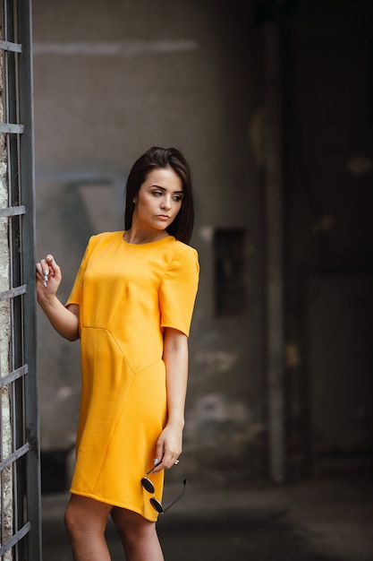 Jolie femme de mode en robe orange posant près du mur blanc