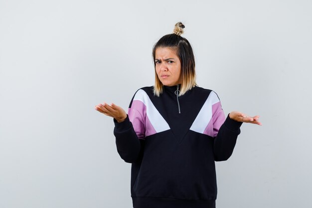 Jolie femme montrant un geste impuissant en sweat-shirt et l'air mécontent