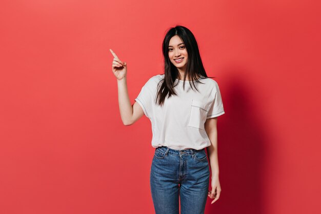 Jolie femme en pantalon en denim montre le doigt à placer pour le texte sur le mur rouge