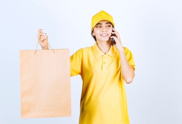 Une jolie femme parlant au téléphone et tenant un sac en papier kraft vierge marron.