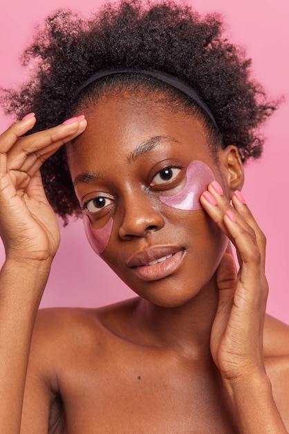 Une jolie femme à la peau foncée aux cheveux bouclés applique des patchs de collagène sous les yeux pour éliminer les cernes