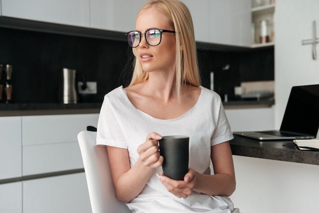 Jolie femme pensive avec tasse de thé assis dans la cuisine