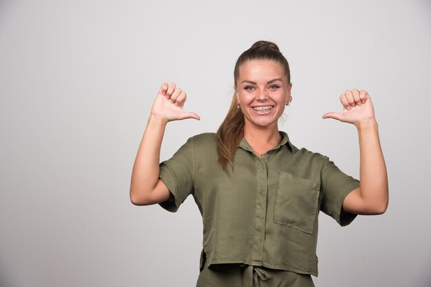 Jolie femme pointant sur elle-même sur un mur gris.