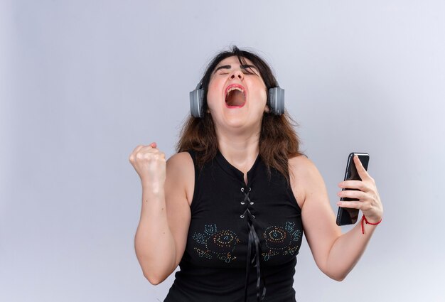 Jolie femme portant un chemisier noir à heureux pour la victoire tenant le téléphone