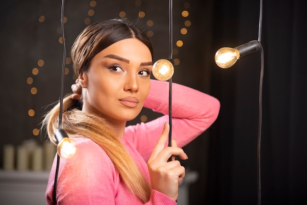 Une jolie femme en pull posant près de lampes lumineuses.