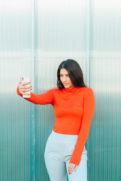 jolie femme regardant écran de téléphone portable debout contre le mur