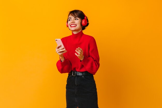 Jolie femme en riant tenant le smartphone sur le mur jaune