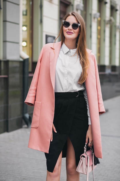 Jolie femme riche souriante élégante marche rue de la ville en manteau rose