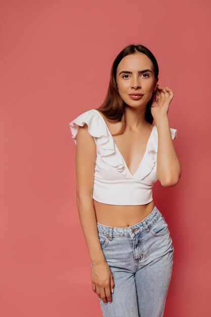 Jolie femme romantique en t-shirt blanc et jeans posant sur un mur rose