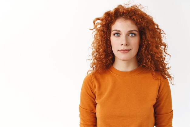 Jolie femme rousse debout seule fond blanc porter un pull orange yeux bleus regardant la caméra sincère et fidèle souriant excité participer à une campagne de promotion intéressante