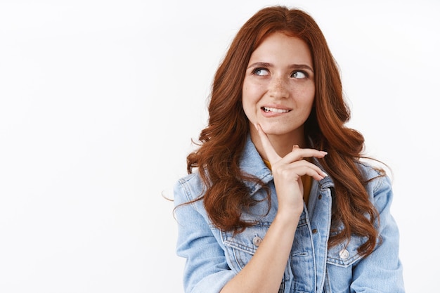 Photo gratuite jolie femme rousse impertinente en veste en jean, l'air curieuse, mordant la lèvre inférieure de la tentation, toucher le menton, regarder de côté en réfléchissant, en pensant à quel ordre, en restant pensif