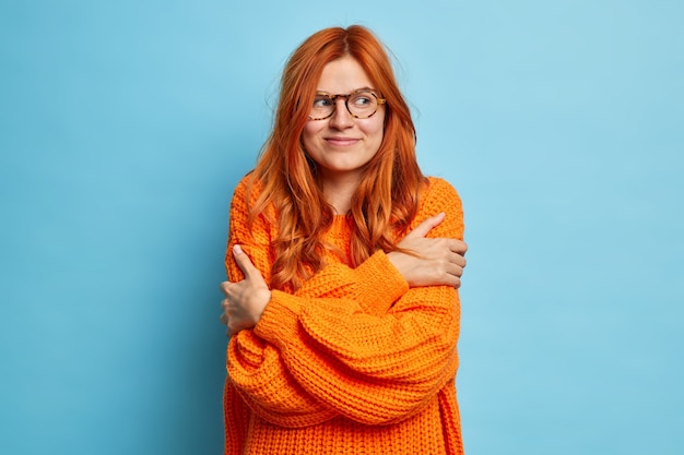 Jolie femme rousse qui s'embrasse aime que son nouveau pull orange tricoté soit satisfait à droite.