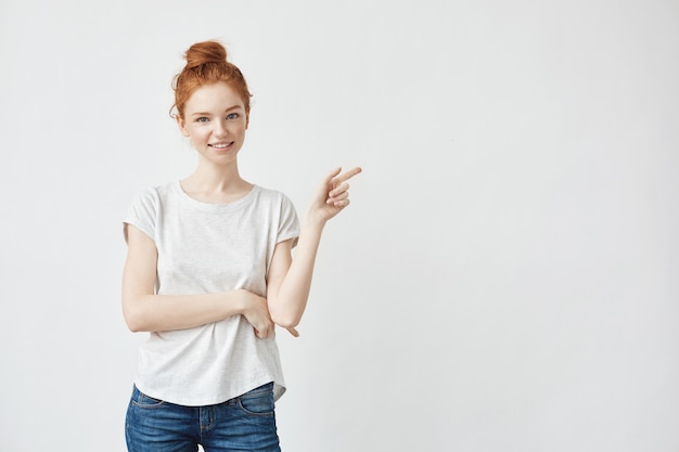 Jolie femme rousse avec des taches de rousseur souriant pointant le doigt droit sur blanc.