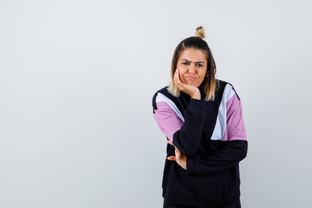 Jolie femme se penchant la tête sur la main en sweat-shirt et l'air mécontent.