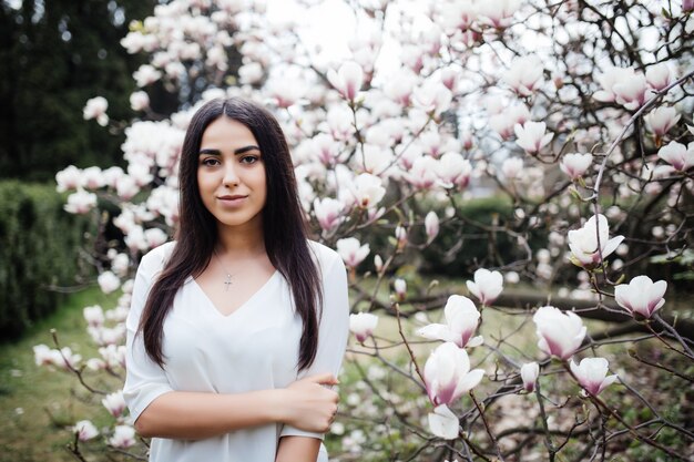 Jolie femme se promène dans le jardin de printemps, apprécie le parfum des magnolias en fleurs