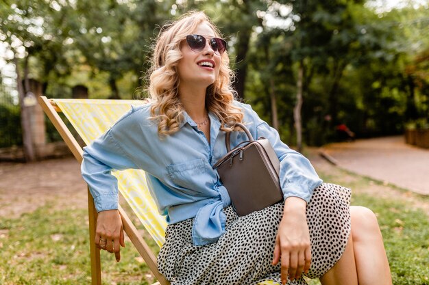 Jolie femme souriante blonde assise dans une chaise longue en tenue d'été