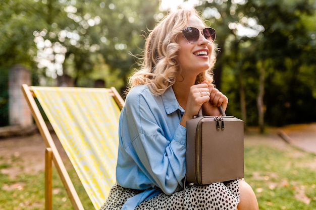 Jolie femme souriante blonde assise dans une chaise longue en tenue d'été