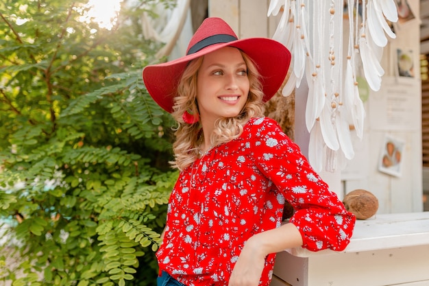 Jolie femme souriante blonde élégante en chapeau rouge paille et chemisier tenue de mode d'été café