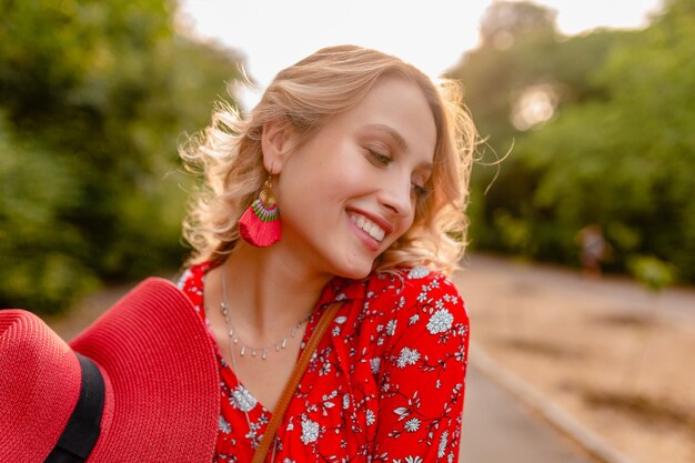 Jolie femme souriante blonde élégante en chapeau rouge de paille et tenue de mode d'été chemisier