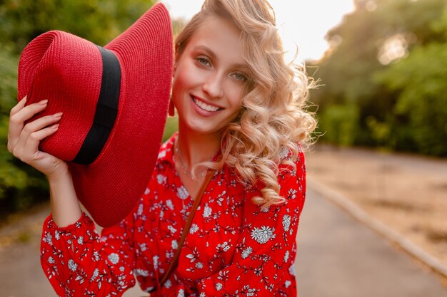 Jolie femme souriante blonde élégante en chapeau rouge de paille et tenue de mode d'été chemisier