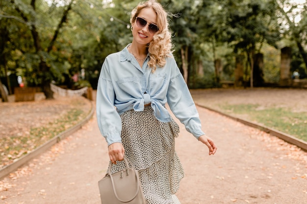 Jolie femme souriante blonde marchant dans le parc en tenue d'été