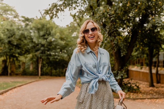 Jolie femme souriante blonde qui marche dans le parc en tenue élégante