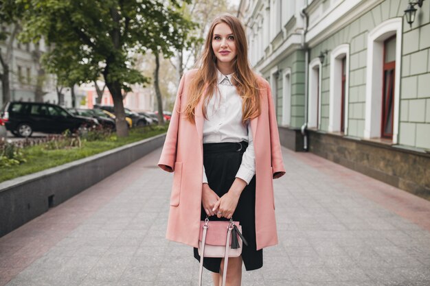 Jolie femme souriante élégante marche rue de la ville en manteau rose