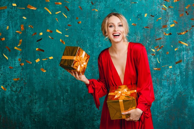 Jolie femme souriante heureuse en robe rouge élégante célébrant Noël et nouvel an avec des cadeaux