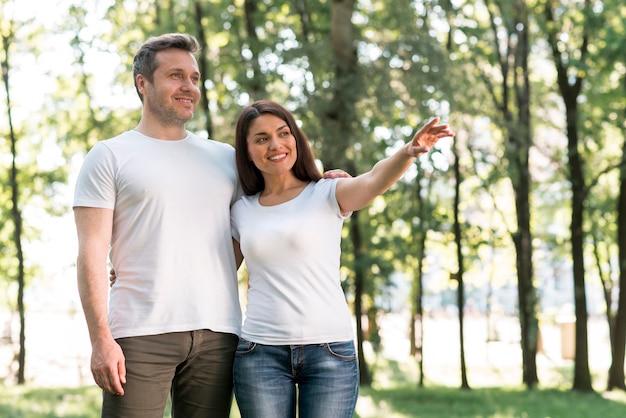 Jolie femme souriante montrant quelque chose à son mari debout dans le parc