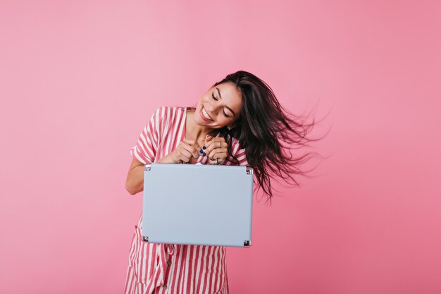 Jolie femme avec un sourire blanc comme neige brillant joue les cheveux. Plan d'un mannequin européen bronzé en tenue d'été avec un bagage à main.