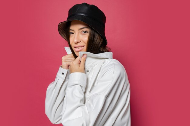 Jolie femme avec un sourire parfait habillé en casquette élégante et veste blanche posant sur fond rose. Isoler.