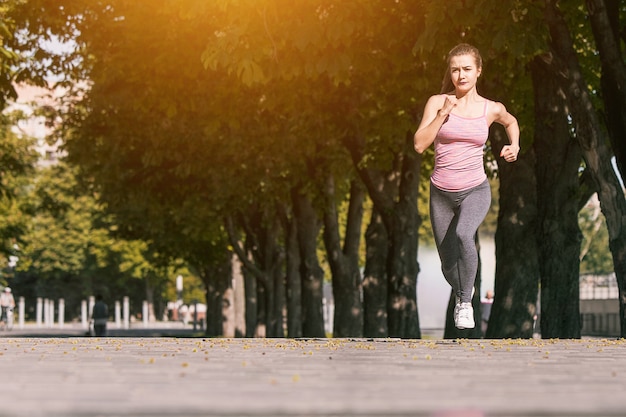 Jolie femme sportive jogging au parc dans la lumière du lever du soleil