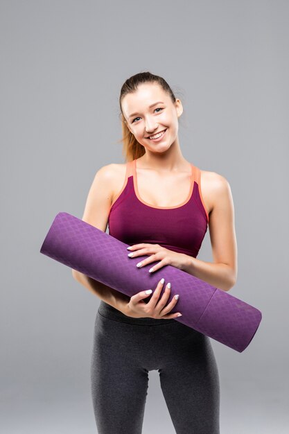 Jolie femme sportive tenant un tapis de yoga avant ou après les cours de fitness isolés