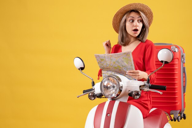 jolie femme surprise au chapeau de panama sur un cyclomoteur avec une valise rouge tenant une carte