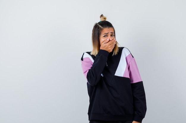 Jolie femme en sweat-shirt fermant la bouche avec la main et ayant l'air horrifiée