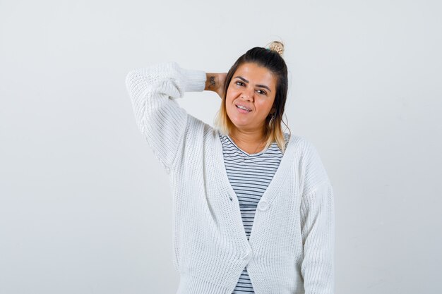 Jolie femme tenant la main derrière la tête en t-shirt, cardigan et fière.