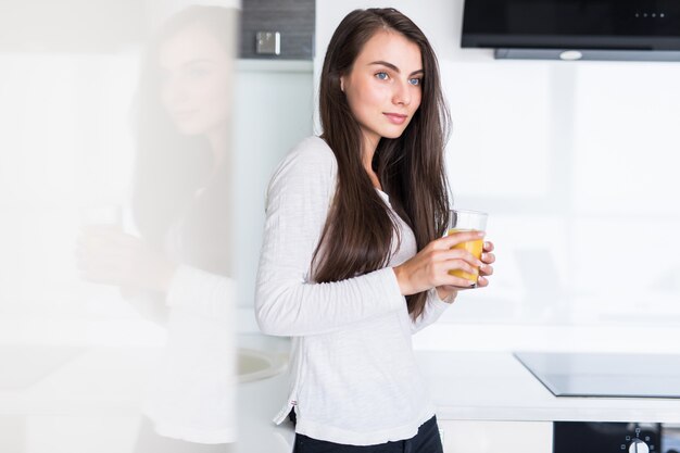 Jolie femme tenant un verre de jus d'orange en se tenant debout dans la cuisine