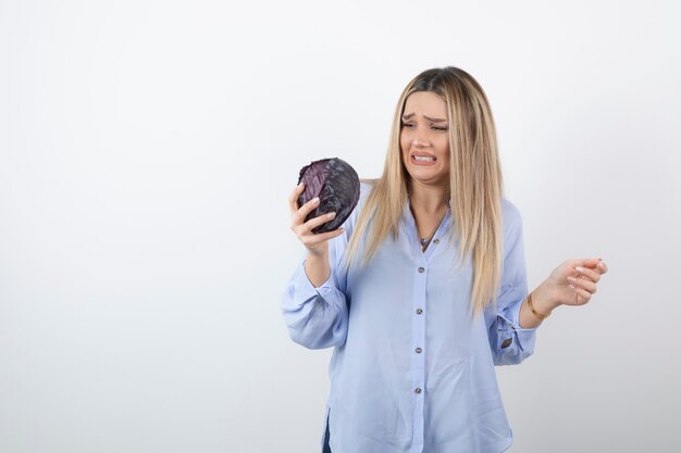 Jolie femme en tenue bleue regardant le chou violet sur un mur blanc.