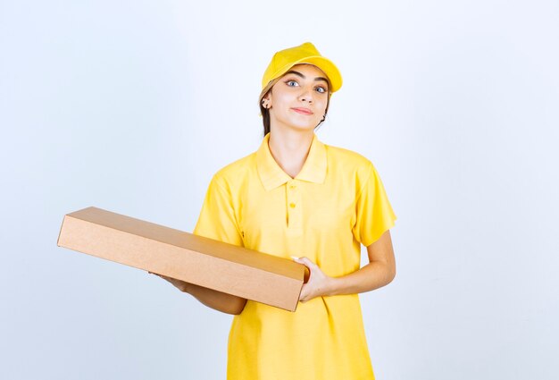 Une jolie femme en uniforme jaune tenant une boîte de papier kraft vierge marron.