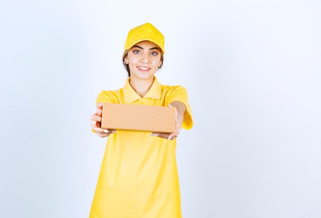 Une jolie femme en uniforme jaune tenant une boîte de papier kraft vierge marron.