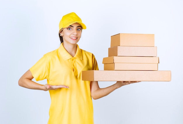 Une jolie femme en uniforme jaune tenant des boîtes de papier kraft vierge marron.