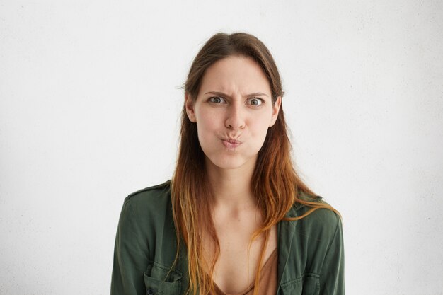 Jolie femme en vêtements décontractés verts bouder. Femme irritée faisant la grimace en regardant fixement.