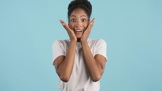 Jolie fille afro-américaine excitée en T-shirt blanc étonnamment regardant à huis clos sur fond coloré Wow expression