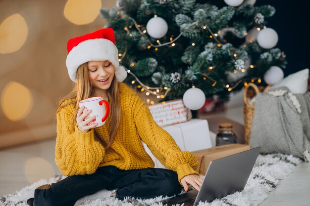 Jolie fille à l'aide d'ordinateur par arbre de Noël