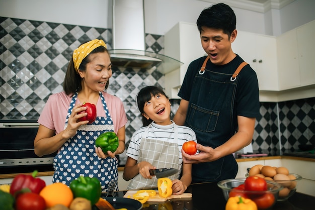 Une jolie fille aide ses parents à couper des légumes et souriant tout en cuisinant ensemble dans la cuisine