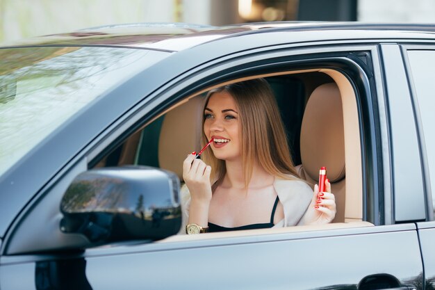 Jolie fille appliquant le rouge à lèvres dans une voiture