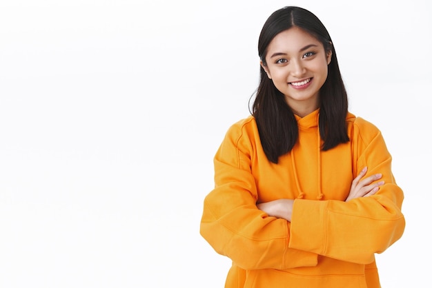 Une jolie fille asiatique habile se sent en confiance pour postuler à un nouvel emploi après avoir obtenu son diplôme, croise les mains sur la poitrine comme un professionnel et souriante, facile à gérer les tâches professionnelles debout sur fond blanc Espace de copie