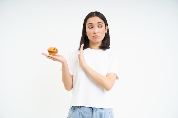 Photo gratuite jolie fille asiatique avec volonté refuse le cupcake reste au régime isolé sur fond blanc