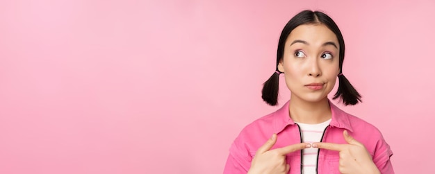 Photo gratuite jolie fille asiatique vous donnant un cadeau dans une boîte en forme de coeur embrassant et souriant concept de vacances et de célébration debout sur fond rose