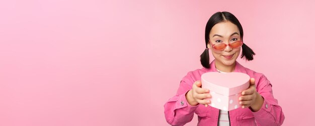 Jolie fille asiatique vous donnant un cadeau dans une boîte en forme de coeur embrassant et souriant concept de vacances et de célébrités